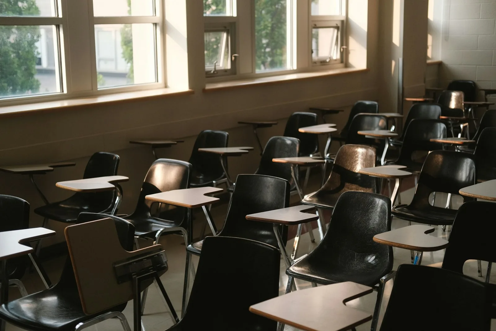 Empty elementary classroom with desks and chairs beside a row of windows